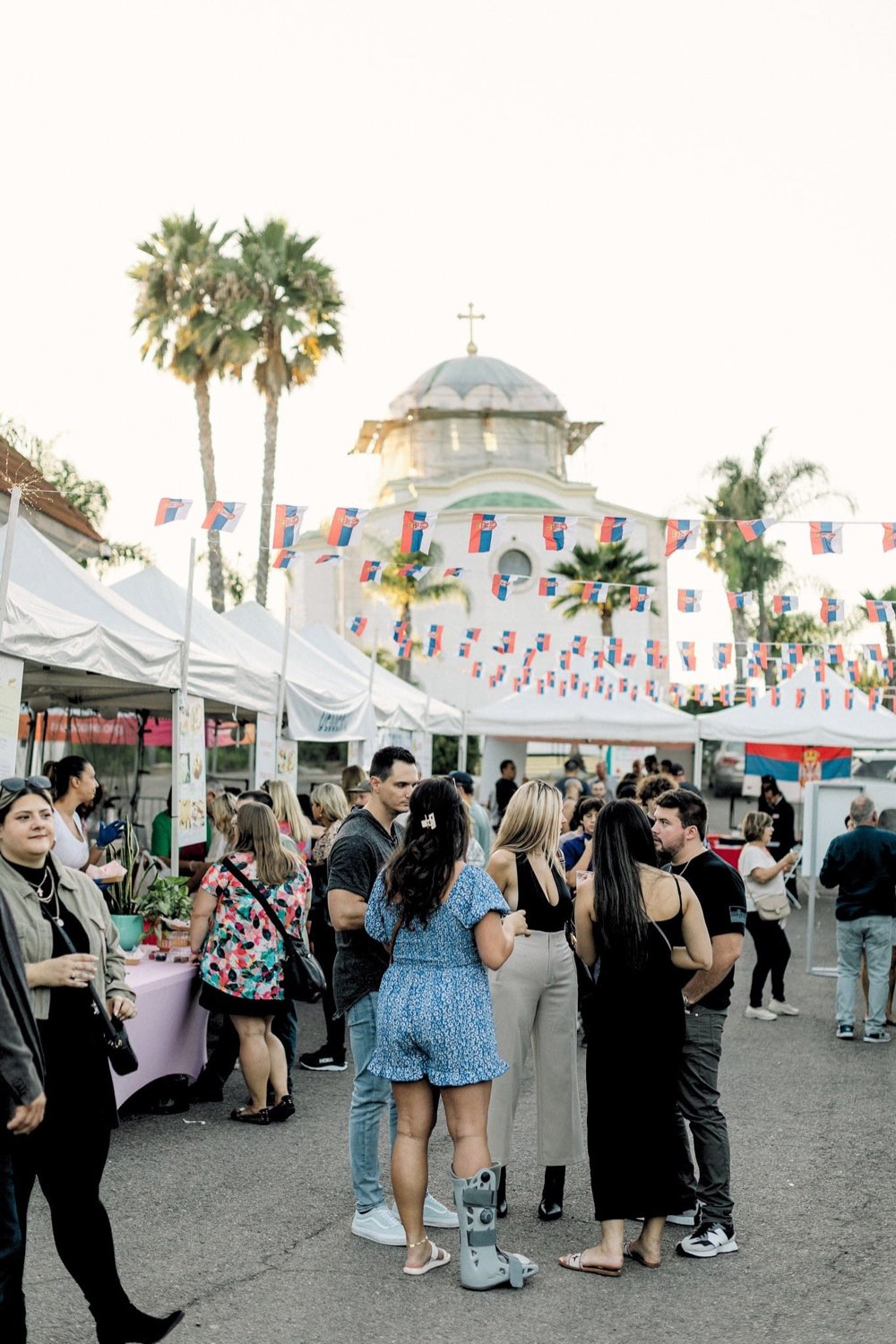 Festivalgoers gathered under Serbian flag bunting at the San Marcos Serb Fest, with Saint Petka's domed church behind